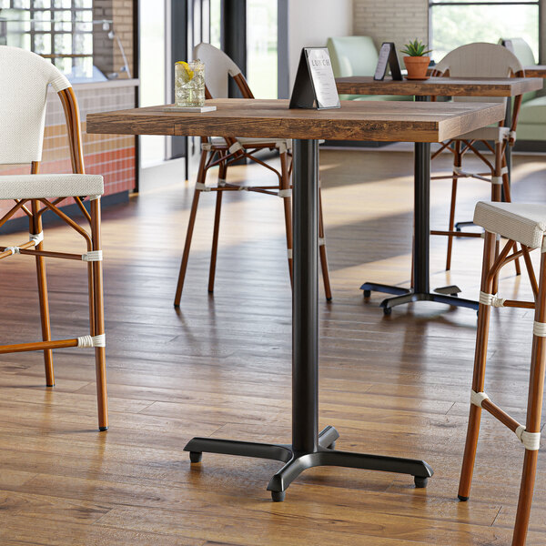 A Lancaster Table & Seating black cast iron bar height table base on a wooden table in a restaurant.