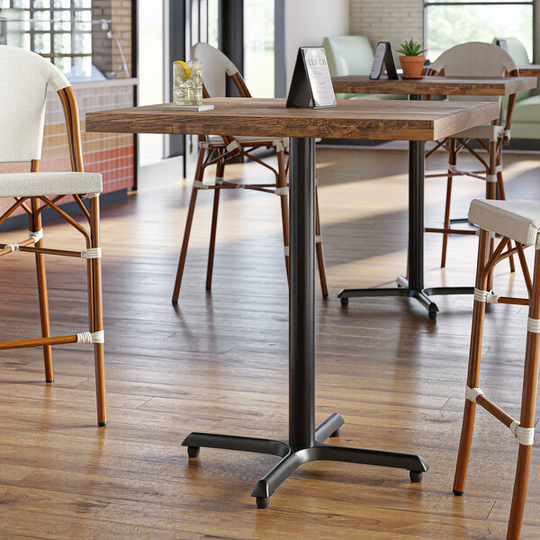 A Lancaster Table & Seating black cast iron bar height table base with FLAT Tech levelers on a restaurant table.