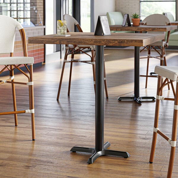 A Lancaster Table & Seating cast iron bar height table base with self-leveling feet on a wooden table in a restaurant dining area.