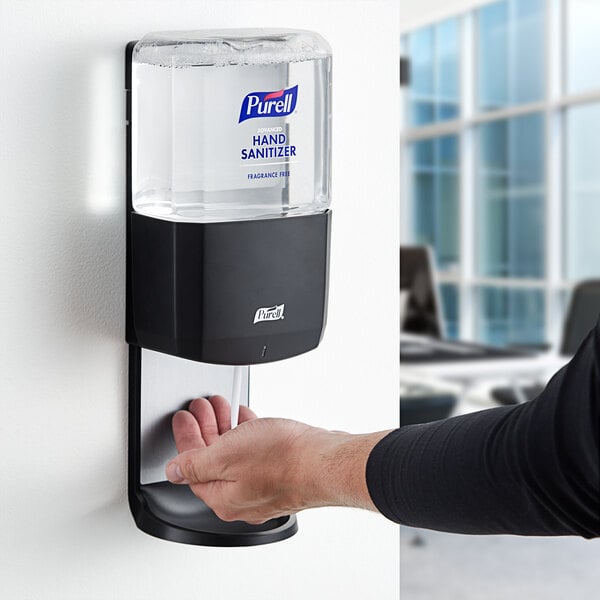 A person using a Purell automatic hand sanitizer dispenser.