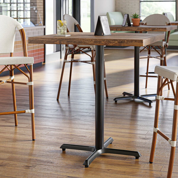 A Lancaster Table & Seating black cast iron bar height table base with chairs around it.