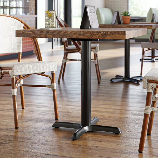 A Lancaster Table & Seating black cast iron table base with self-leveling feet under a restaurant table with chairs.