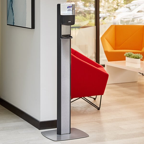 A Purell black automatic hand sanitizer dispenser on a graphite floor stand in a corporate office cafeteria.