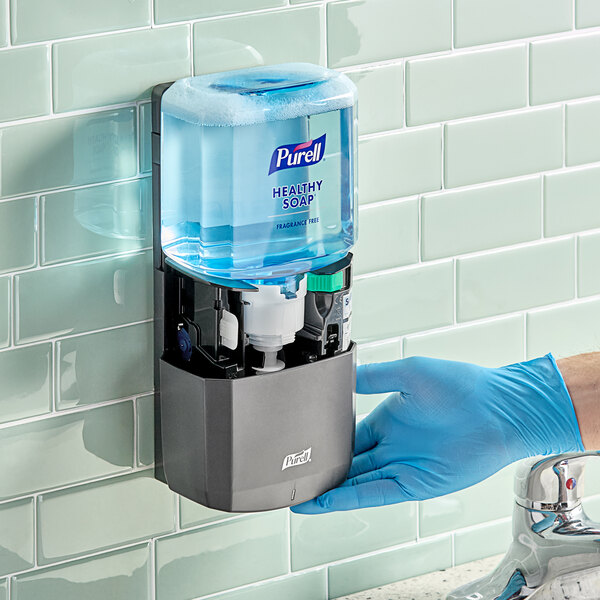 A person in blue gloves using a Purell Healthy Soap dispenser.