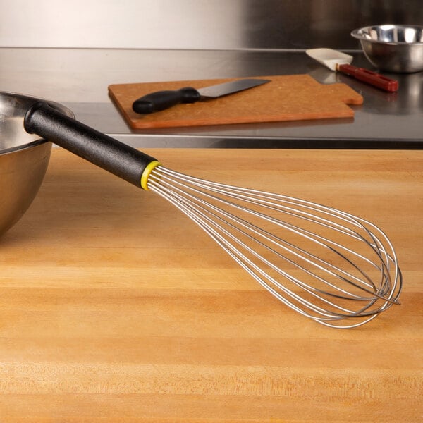 A Matfer Bourgeat stainless steel piano whisk in a bowl on a wood surface.