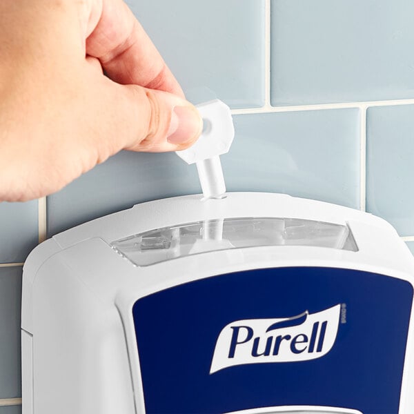 A hand using a white Purell dispenser key to refill a wall-mounted Purell dispenser.