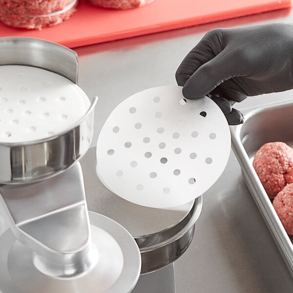 A hand in a black glove uses Choice 5" Perforated Round Patty Paper to shape a meatball.