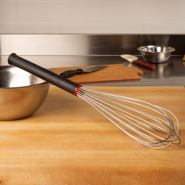 A Matfer Bourgeat stainless steel whisk with an Exoglass handle on a wooden surface.