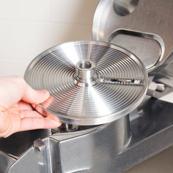 A hand holding a circular metal crimping plate with a knife attached.