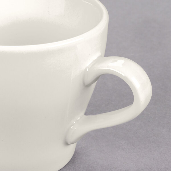 A close-up of a white Tuxton Europa cappuccino mug with a handle.