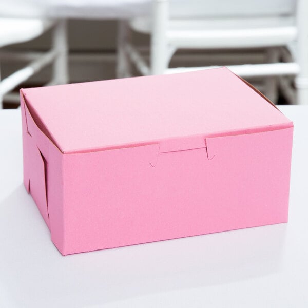 A close-up of a 6 1/2" x 4" x 2 3/4" pink bakery box with a lid on a white surface.