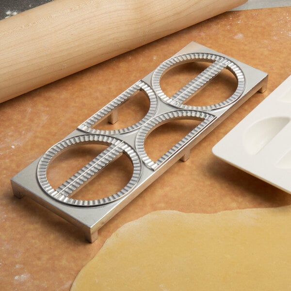 A metal Fox Run dumpling maker and rolling pin on a table.