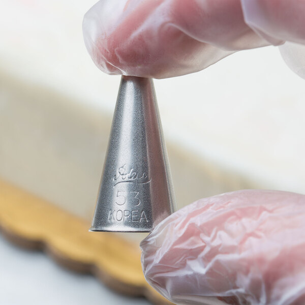A person holding a silver Ateco 53 Cross-Top piping tip.