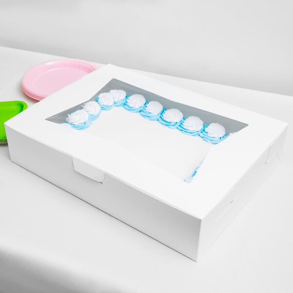 A white rectangular bakery box with a clear window on top, containing a cake decorated with blue and white icing.