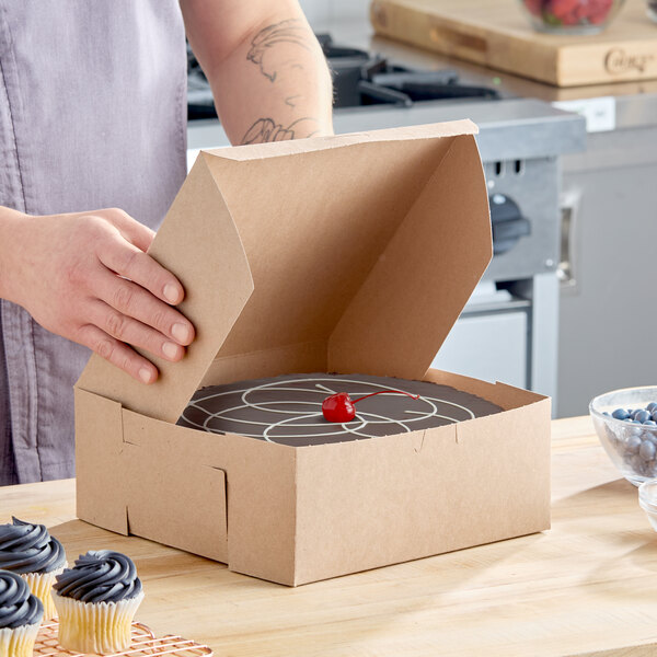 A brown kraft paper bakery box with a cake inside, partially opened on a kitchen counter.