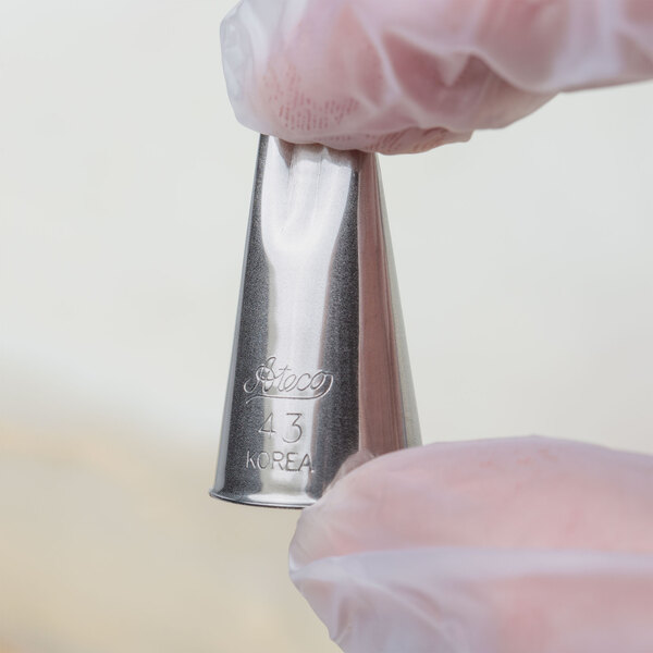 A hand holding a silver metal Ateco 2-hole piping tip.