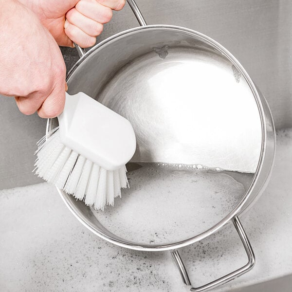 A person cleaning a pot with a Carlisle Sparta white utility brush.