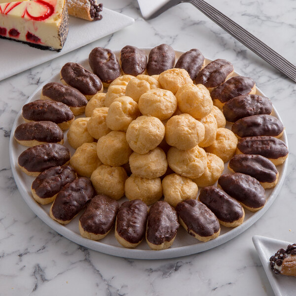 A G.E.T. Enterprises white resin-coated metal serving disc with pastries on a marble surface.