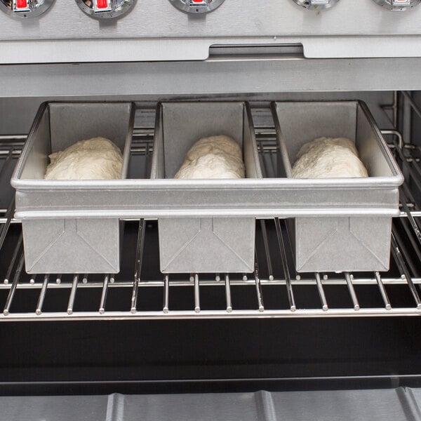 A Chicago Metallic aluminized steel bread loaf pan with 3 loaves of bread inside.
