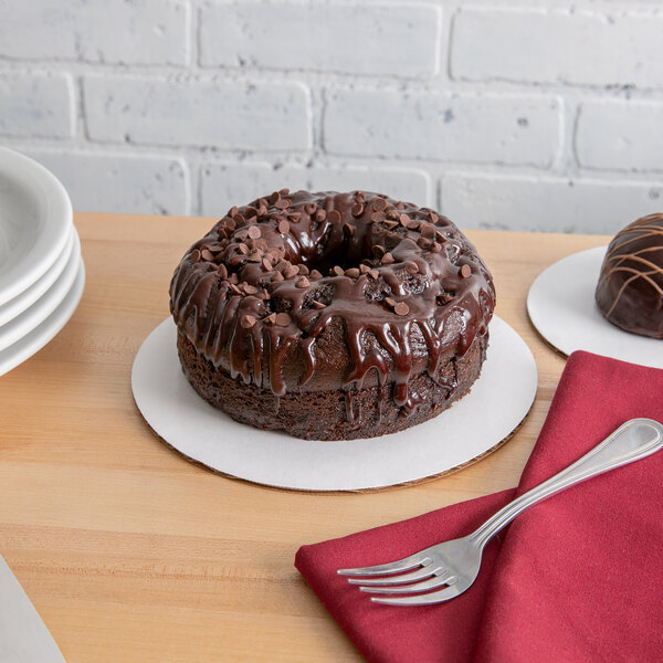 A chocolate cake on a white corrugated cake circle with chocolate chips and drizzle on top with a fork on a table.