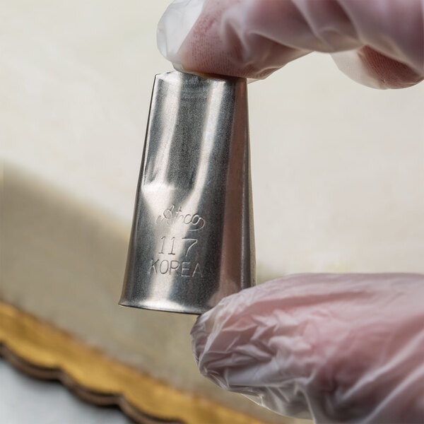 A person wearing gloves using an Ateco rose piping tip on a pastry bag.