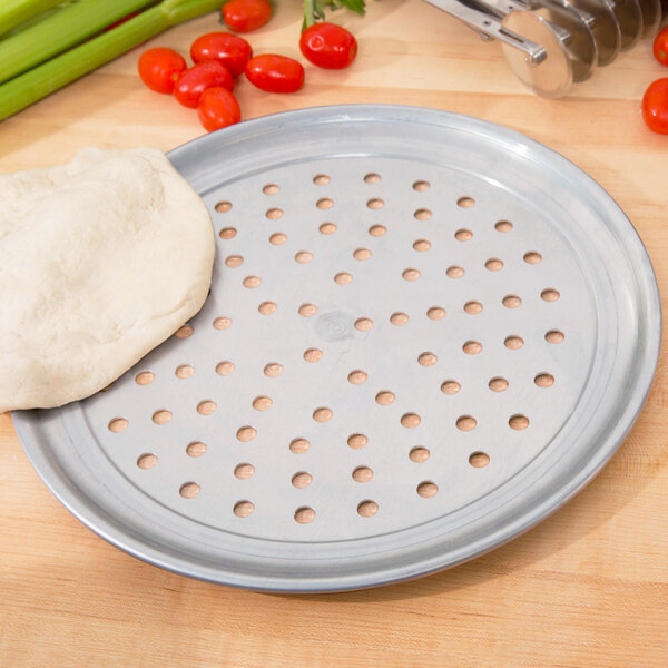 An American Metalcraft aluminum pizza pan with dough on top of it.