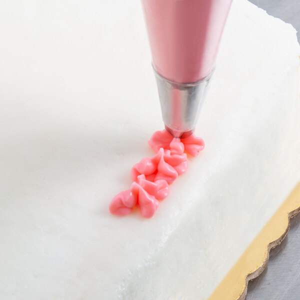 A white cake decorated with pink flowers using an Ateco drop flower piping tip.