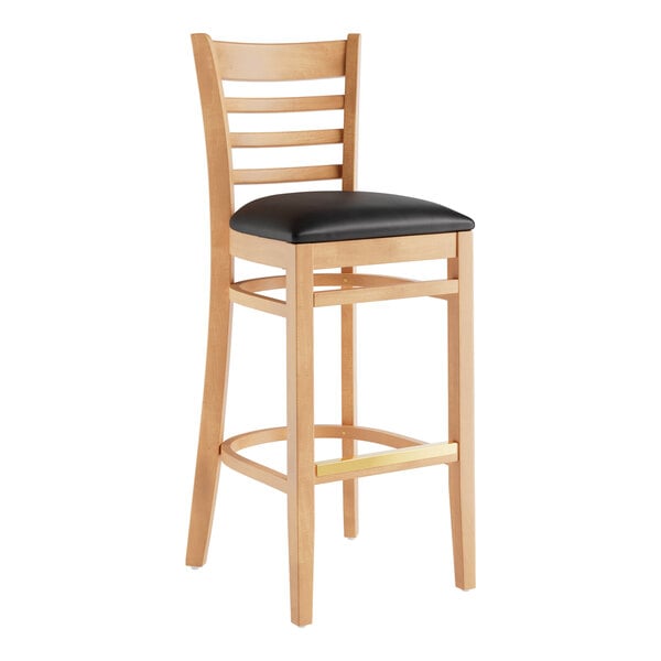A Lancaster Table & Seating wood ladder back bar stool with a black vinyl seat.