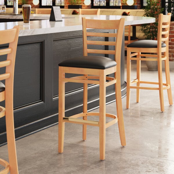 A Lancaster Table & Seating wooden bar stool with a black vinyl seat.