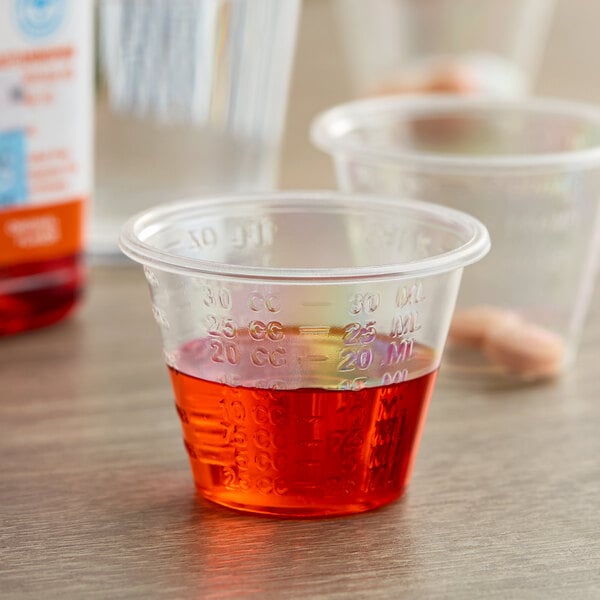 A clear disposable polypropylene medicine cup with graduated measurement markings, partially filled with red liquid.