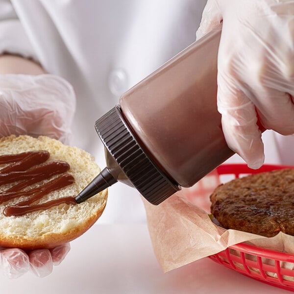 A hand wearing a plastic glove squeezing sauce from a Vollrath Color-Mate squeeze bottle onto a burger bun.