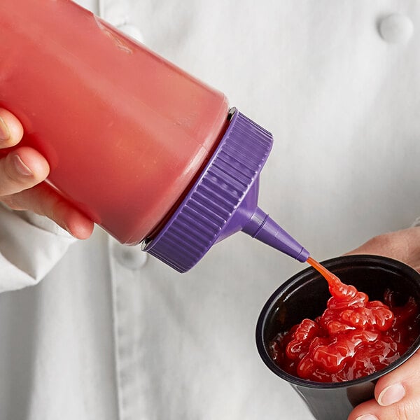 A person pouring sauce from a Vollrath Clear Squeeze Bottle with a purple cap into a cup of food.