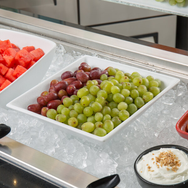 A white G.E.T. Enterprises deep square bowl with grapes in it.