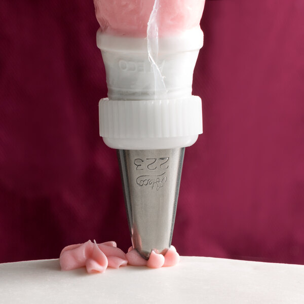 A cake being piped with a white plastic pastry bag using an Ateco Drop Flower piping tip.