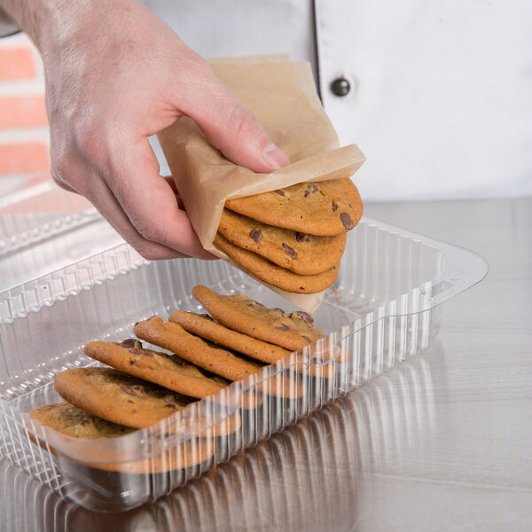 A hand using Bagcraft EcoCraft deli wrap to put chocolate chip cookies into a brown paper bag.