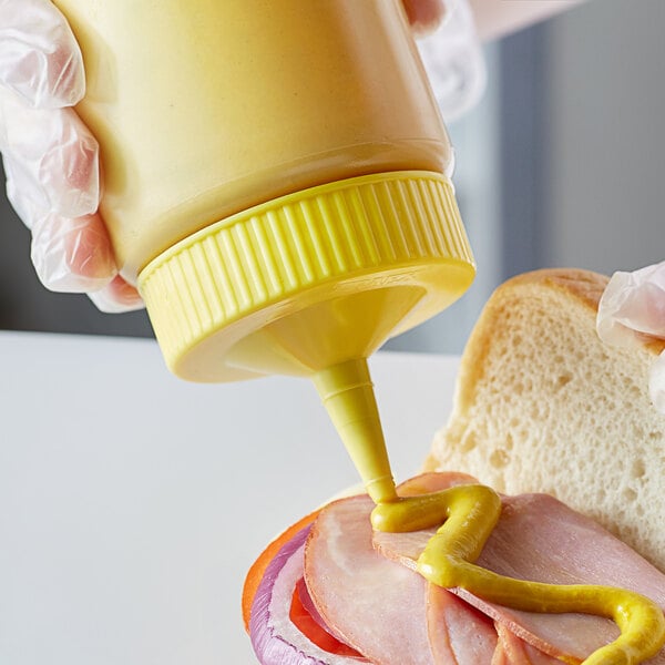 a person pouring mustard onto a sandwich