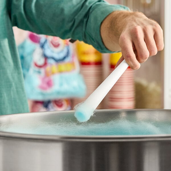 A person spinning blue cotton candy onto a white paper cone over a cotton candy machine.