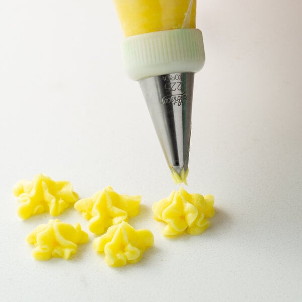 A person using an Ateco drop flower piping tip to make yellow flowers with a pastry bag.