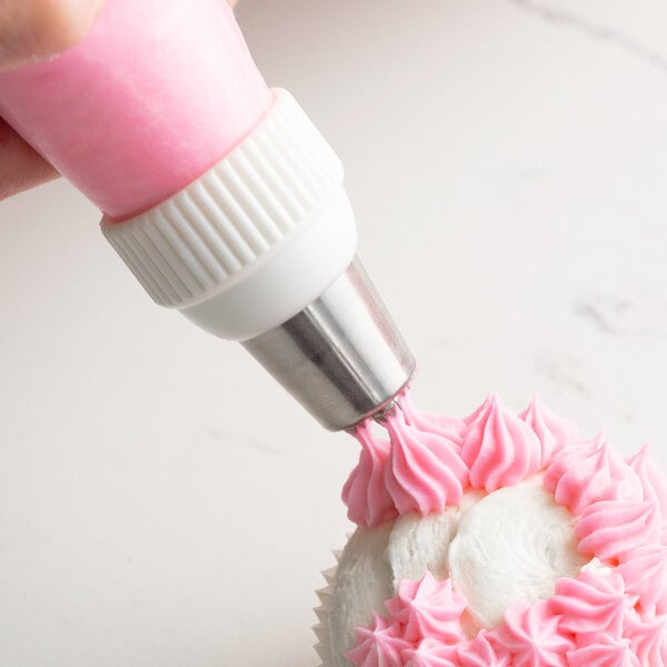 A hand using an Ateco triple star piping tip to pipe pink frosting on a cupcake.