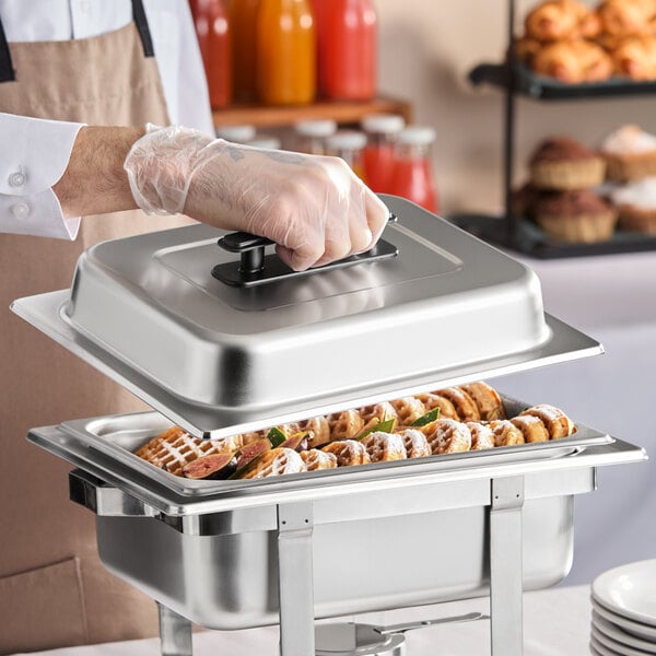 A stainless steel pan with a chafer cover being lifted by a person wearing a glove.