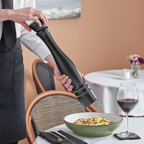 A person using an Acopa matte black wooden pepper mill over a bowl of food.