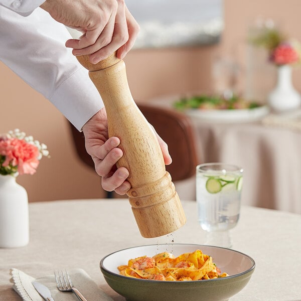 A person grinding Acopa wooden pepper mill over a bowl of pasta.