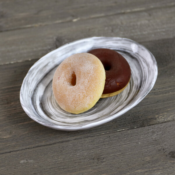 An Elite Global Solutions black oval melamine plate with two donuts on it on a wood table.