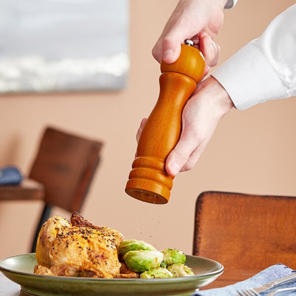 A hand using an Acopa matte brown wooden pepper mill over a plate of food.