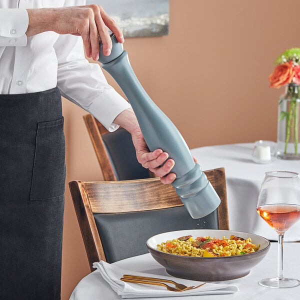 A person holding a Acopa steel blue wooden pepper mill over a bowl of noodles.