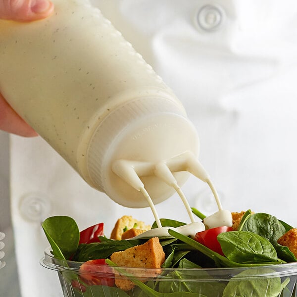 A person using a Vollrath Tri Tip squeeze bottle to pour dressing onto a salad.