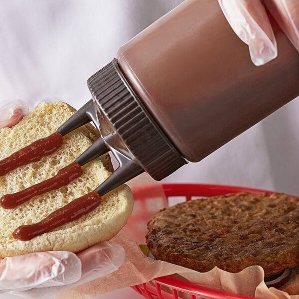 A person using a Vollrath Tri Tip Squeeze Bottle to put ketchup on a hamburger.