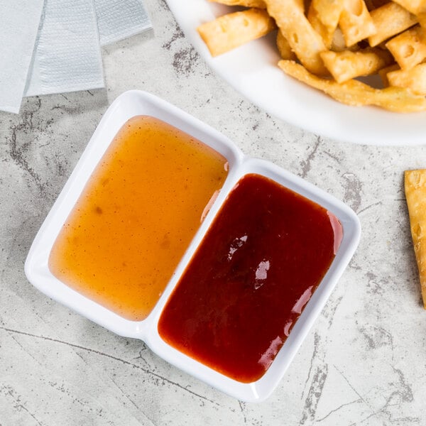 A plate of food with white twin melamine sauce dishes filled with dipping sauce.