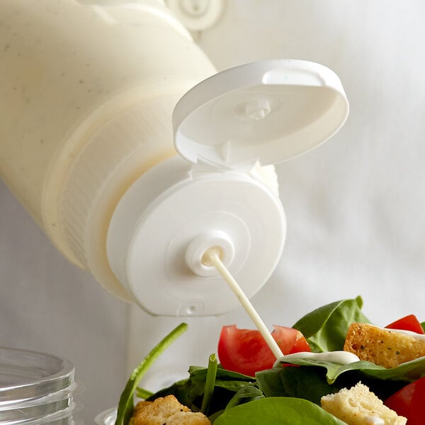 A salad being poured from a Vollrath Traex wide mouth squeeze bottle cap converter onto a salad.
