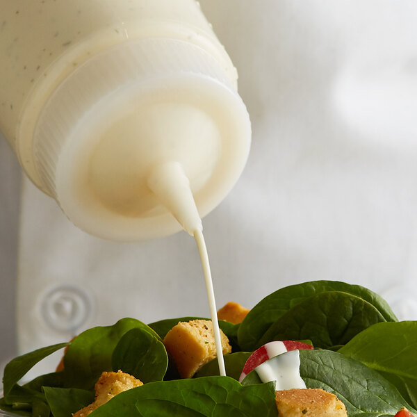 A person using a Vollrath Traex wide mouth bottle cap to pour dressing on a salad.